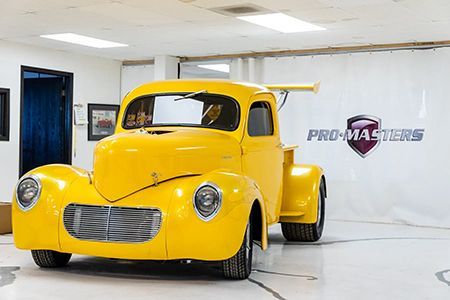 Yellow classic pickup truck with large spoiler, parked in a showroom setting.