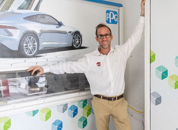 Man in white shirt and khakis poses near a car paint display with PPG logo.