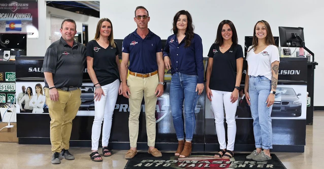 Six people pose in front of a counter with products. Some wear black shirts, jeans, and khakis. The word “PROPERT” is on the mat.