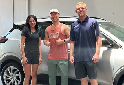 Three people standing in front of a silver SUV with the hatch open. They are smiling. Indoor setting.