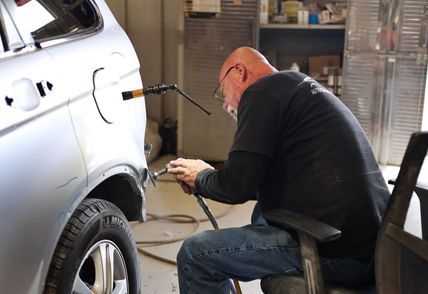 A person repairing a silver car's rear panel in a garage, using a tool.