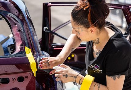 Woman applying film to a car door, spraying it with a bottle.