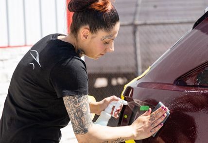 Auto body worker uses a tool to repair a dent on a car's hood in a workshop.