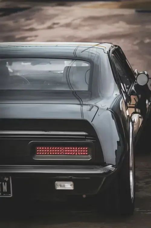 Rear view of a classic black car with a red taillight and a custom license plate.