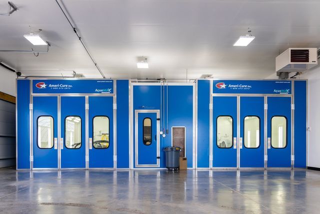 Blue paint booth in a garage, with glass windows, doors, and overhead lights.