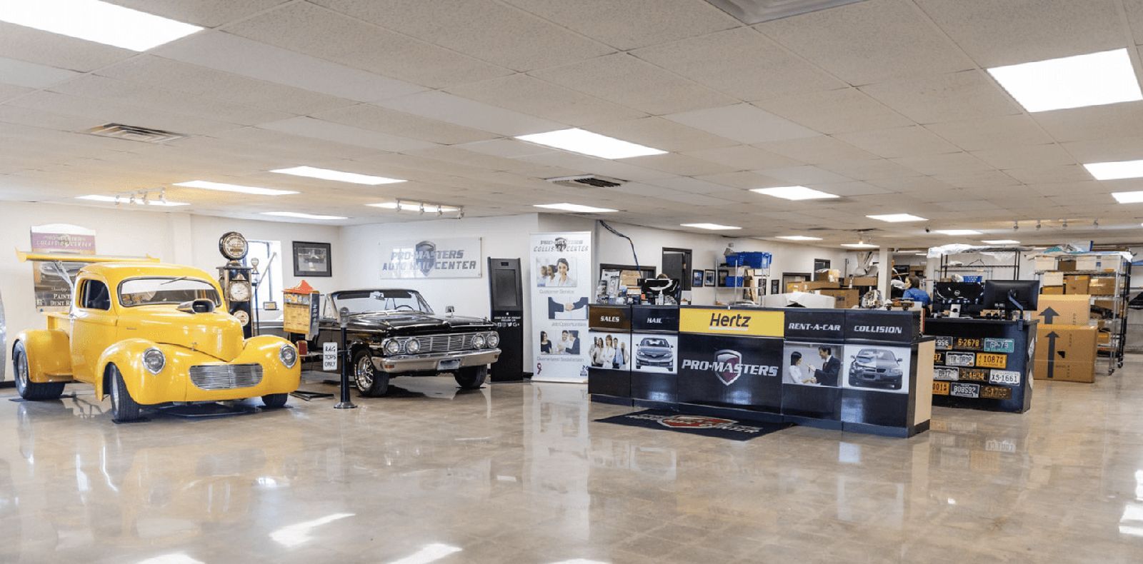 A showroom with a yellow vintage truck, black car, and displays.
