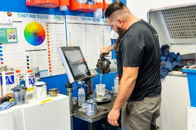 Man mixing paint in a shop, color mixing guide visible.