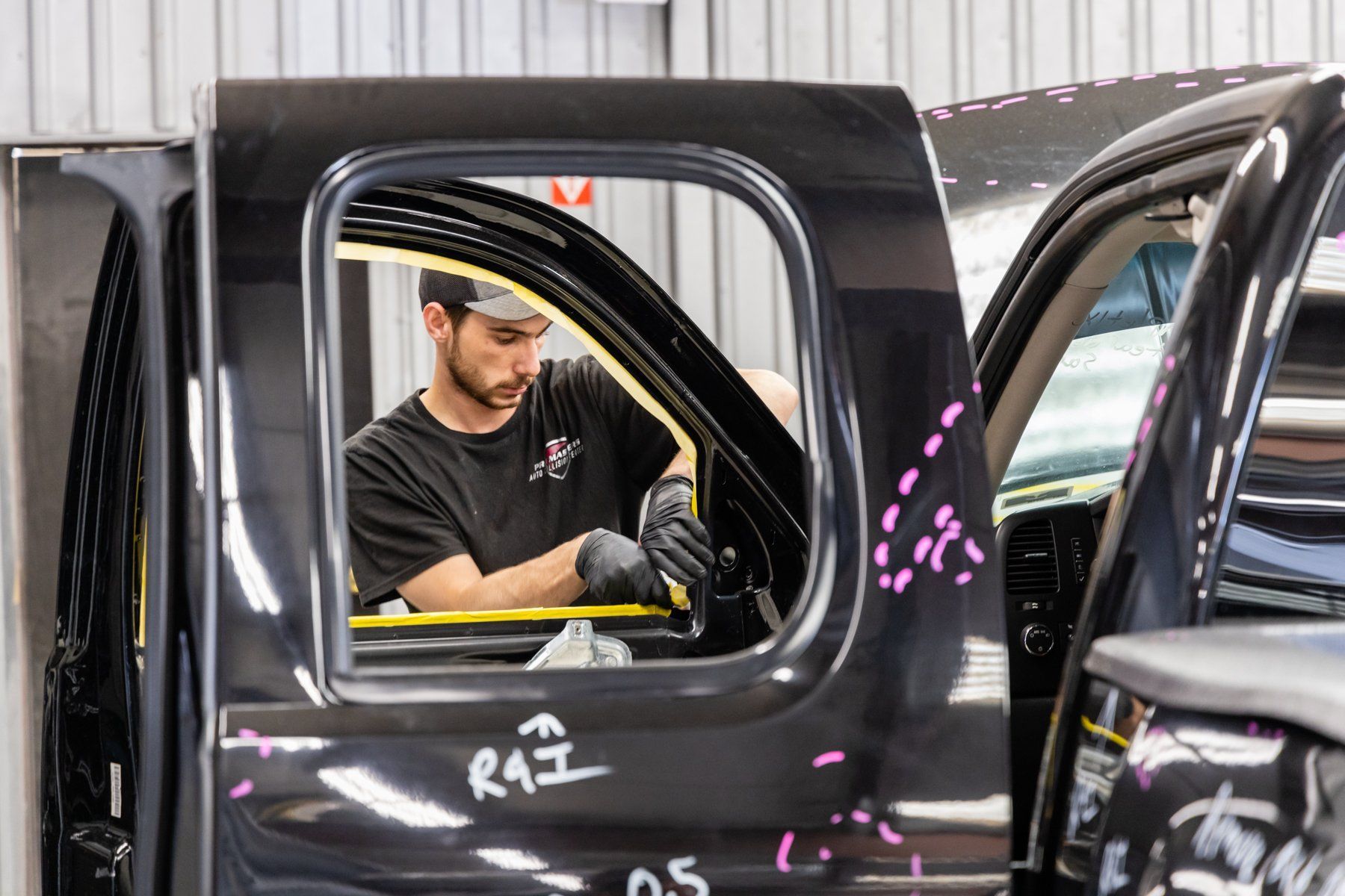 A mechanic working on a black truck door inside a shop.
