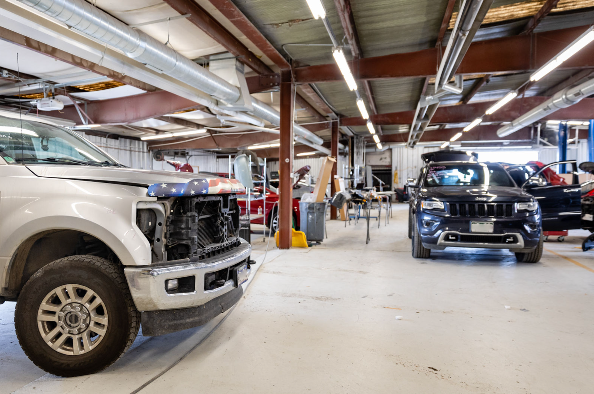 Truck and SUV in auto repair shop with exposed ceiling, fluorescent lights, and tools.