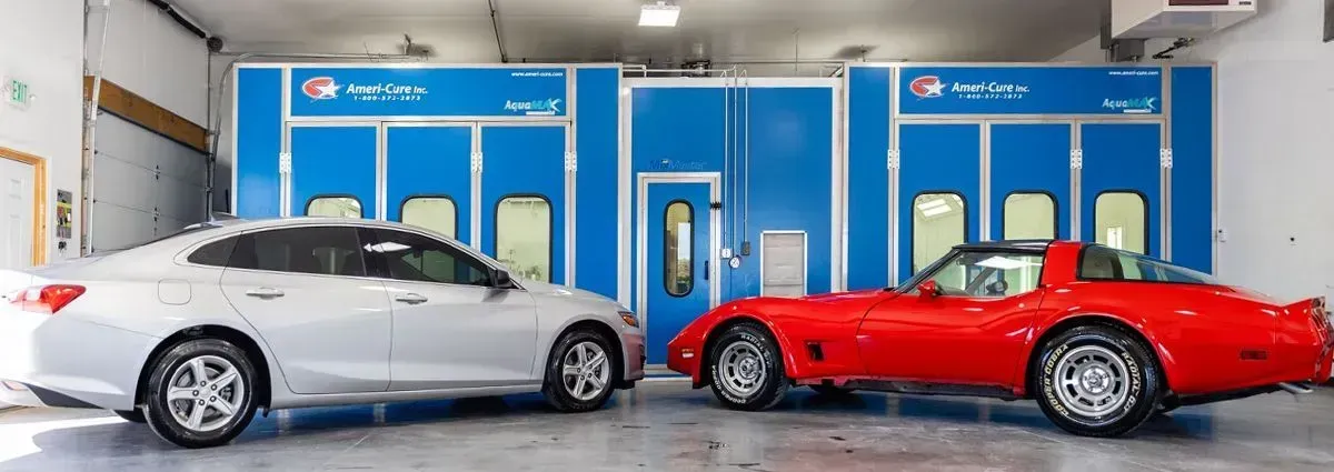 Two sports cars, silver and red, parked outside a blue auto service building