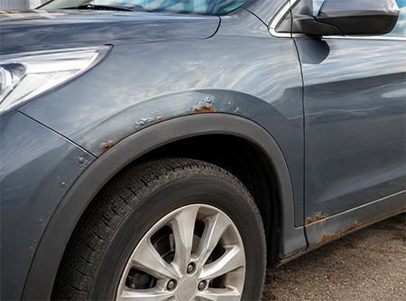 Gray SUV with rust spots and minor body damage near the front wheel well