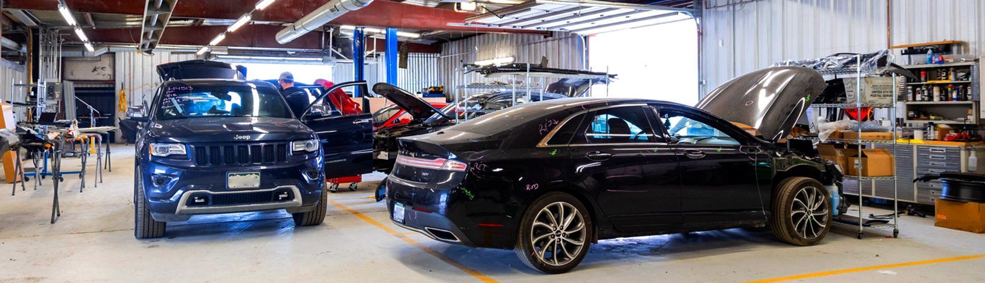 A car repair shop with several vehicles, some with open hoods, and tools.