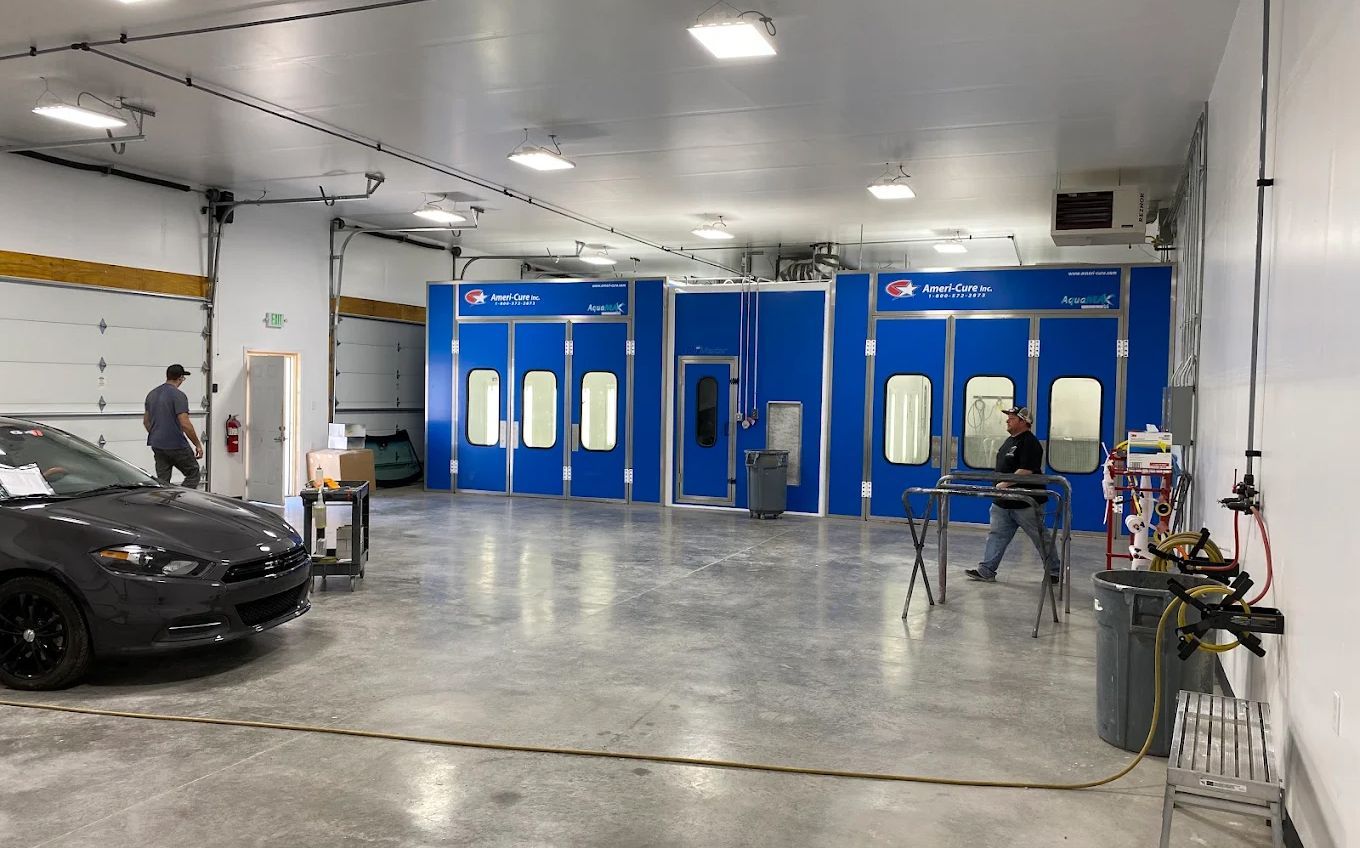 Auto repair shop with blue paint booths, two people, and a black car in the foreground