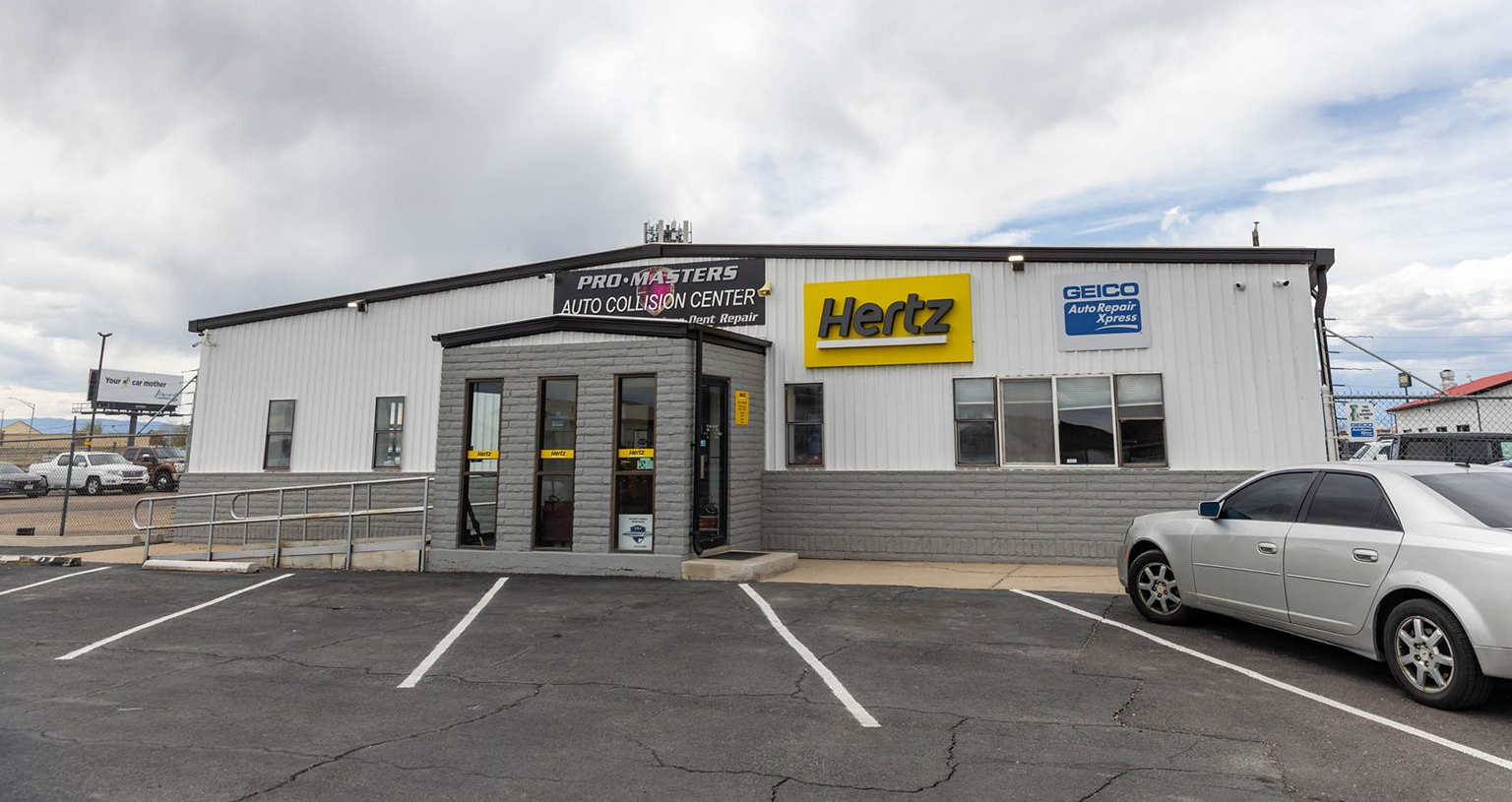 Small commercial building with Hertz sign and parked cars in a mostly empty parking lot
