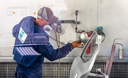 Auto body worker sprays paint on a car door in a paint booth.