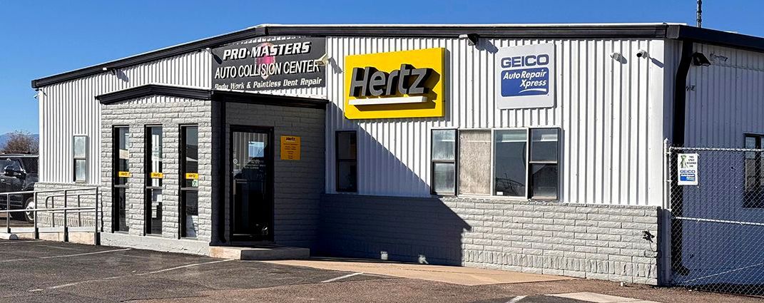 A rental car building. It has a Hertz sign and various other logos. It has a gray stone facade.
