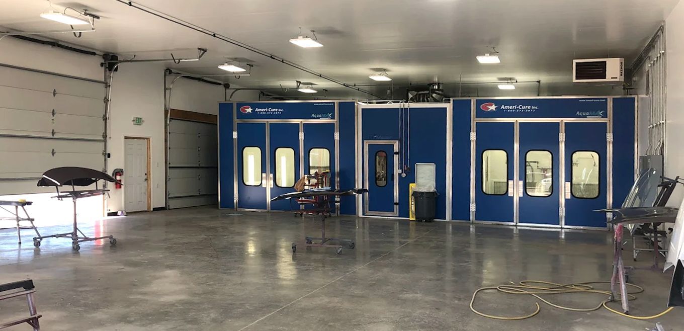 A large, empty auto body shop with spray booths in the center and garage doors on the left.