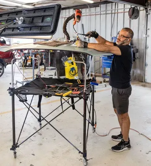 Man working on car part with tools on a table in a workshop.