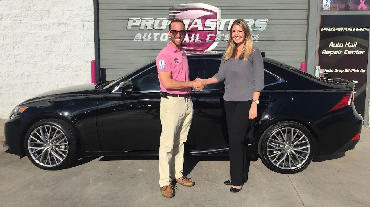 Man and woman shaking hands next to a black car in front of an auto repair shop.