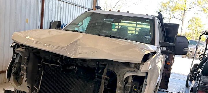A severely damaged white truck in a garage. The front end is smashed.