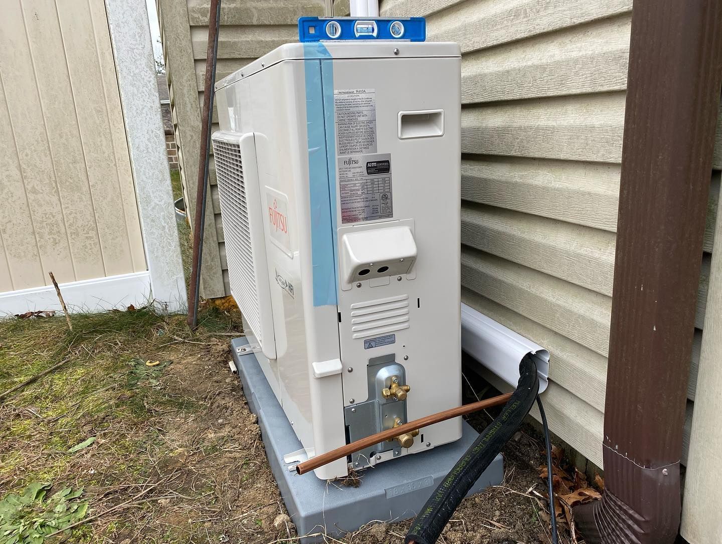 A white air conditioner is sitting on a concrete base next to a house.