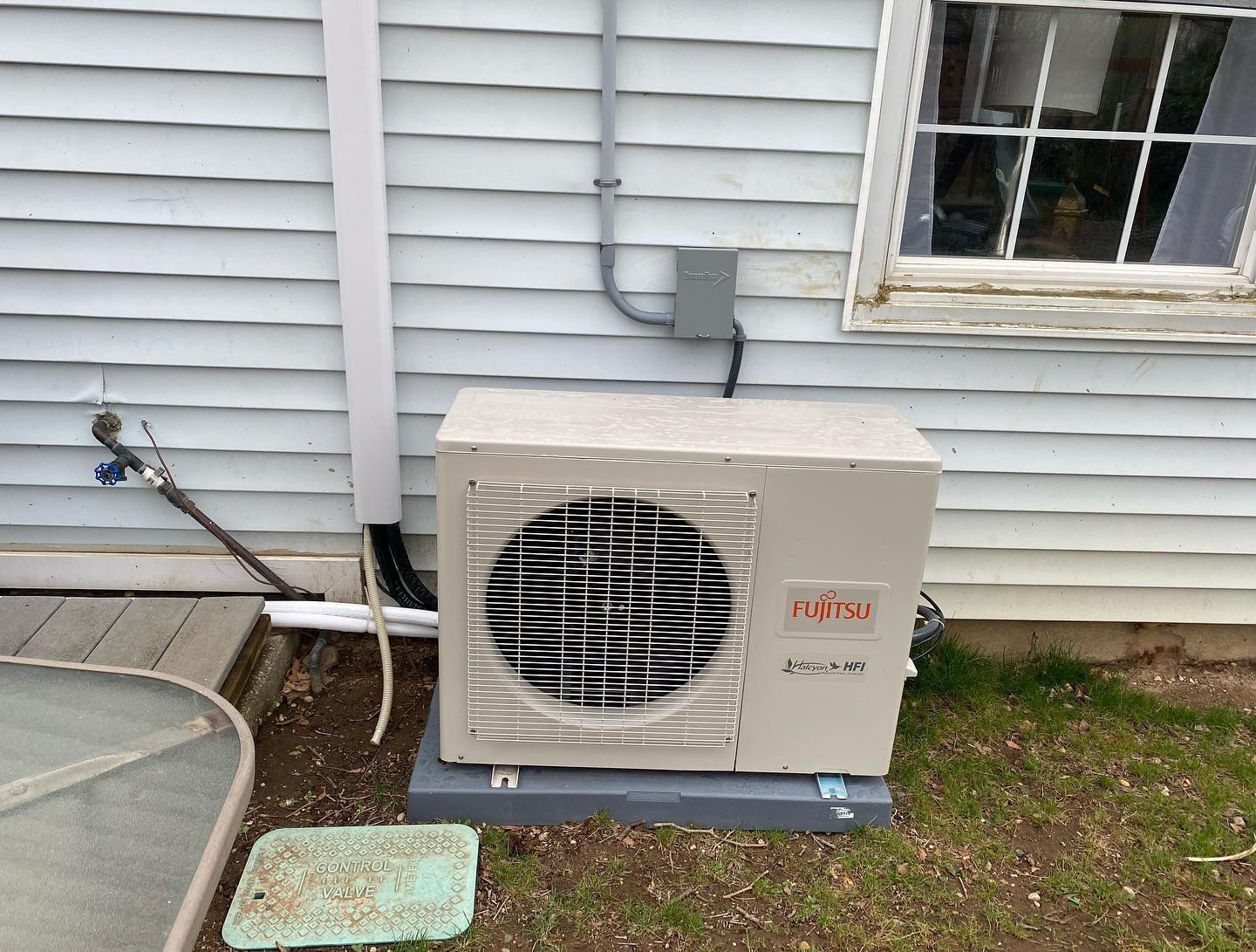 An air conditioner is sitting outside of a house next to a window.