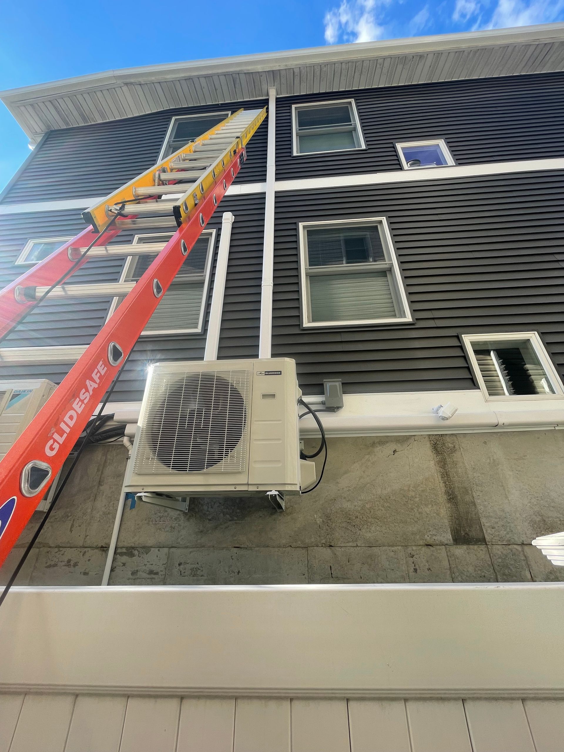 A ladder is sitting on the side of a building next to an air conditioner.