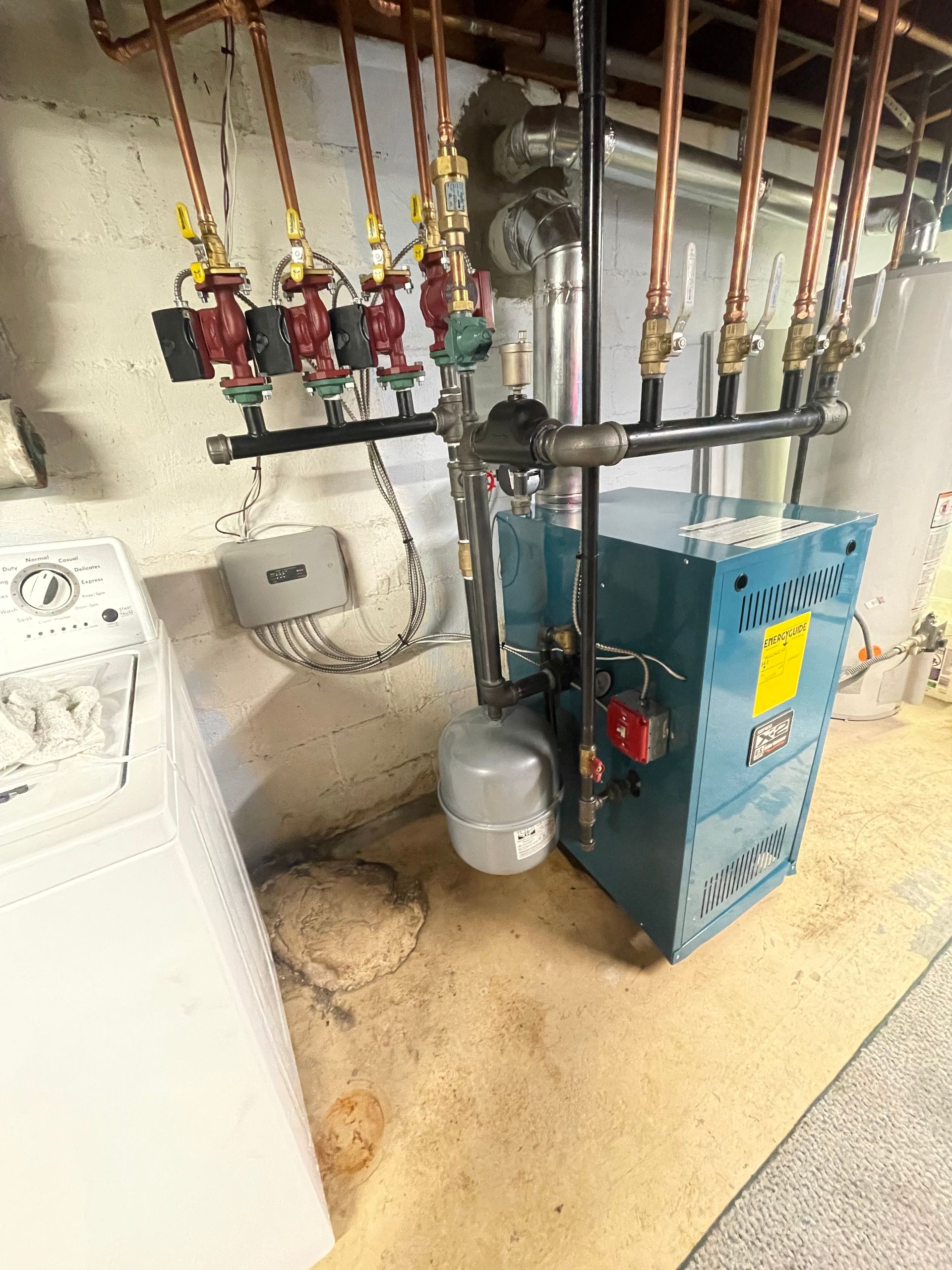 A blue boiler is sitting in a basement next to a washer and dryer.