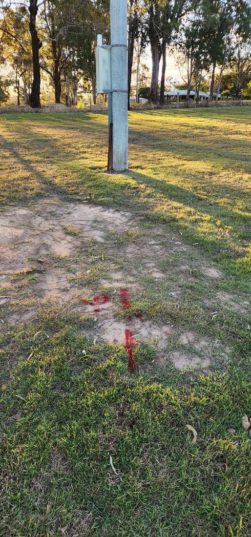 A Metal Utility Pole in a Grassy Area With Red Spray-painted Markings on the Ground — Found It Down Under in Gympie, QLD