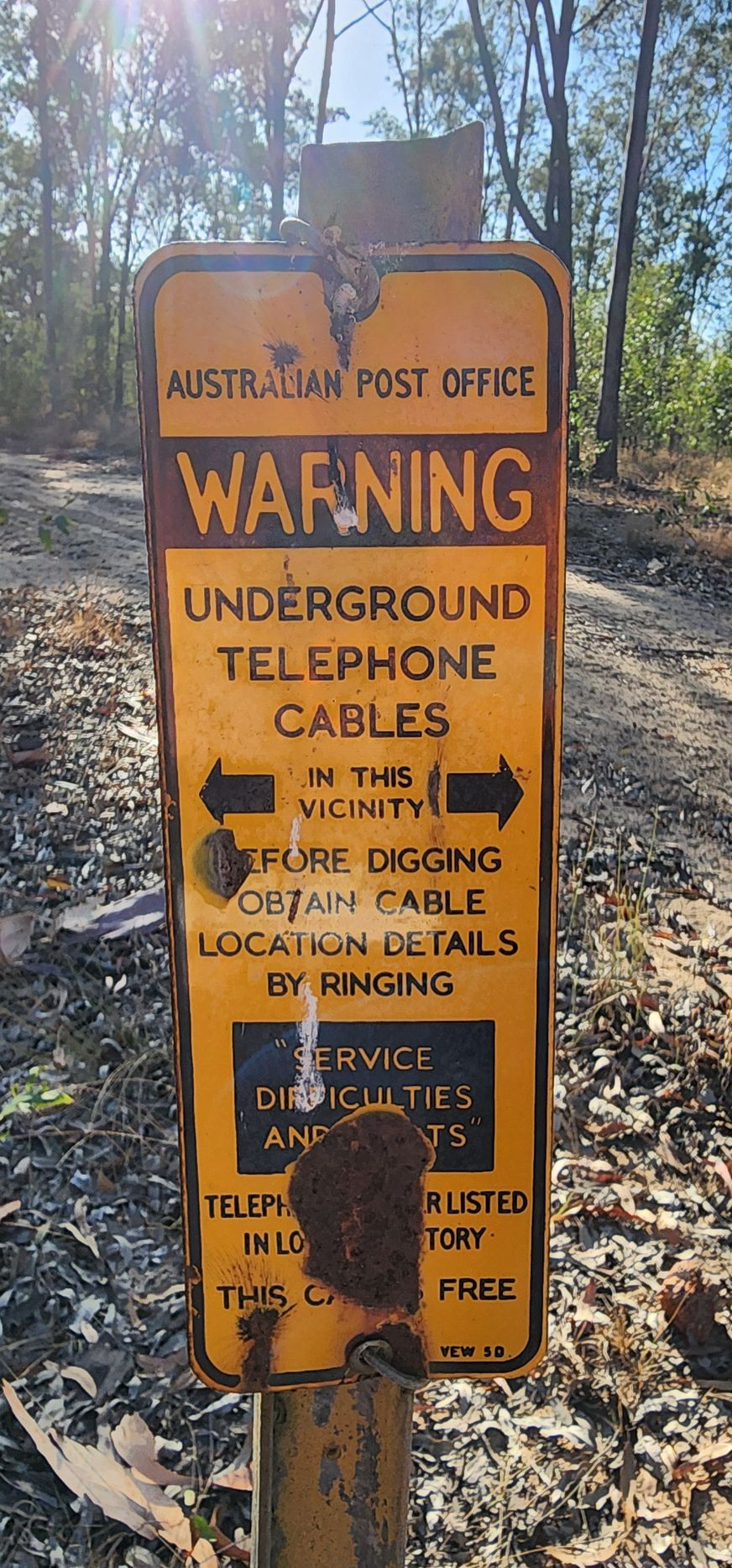 Yellow warning sign for underground telephone cables in a wooded area. Sign has Australian Post Office text.