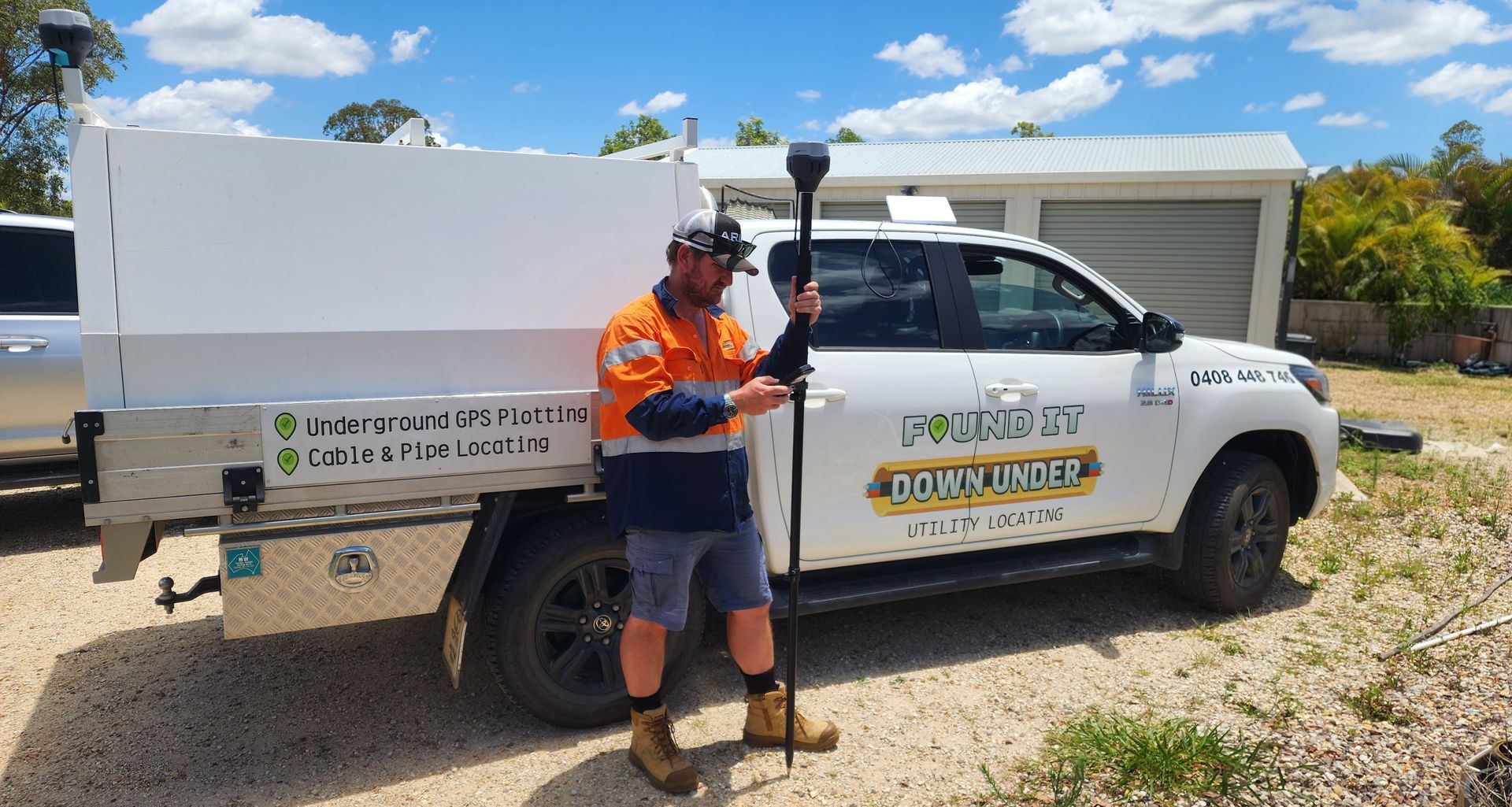 Man in work clothes holding surveying equipment next to a white work truck in front of a house.