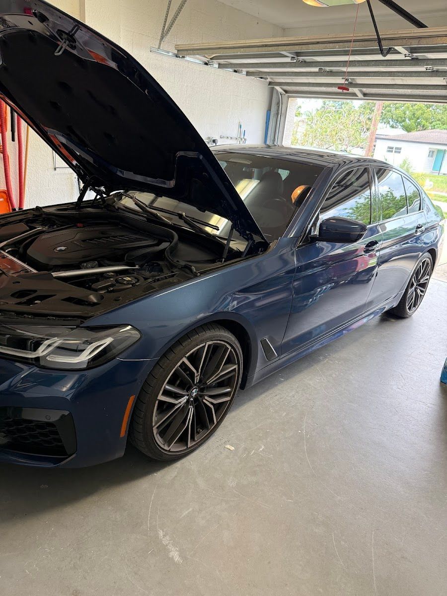 Blue BMW sedan with hood open in a garage, black wheels. | Midnite Tuning