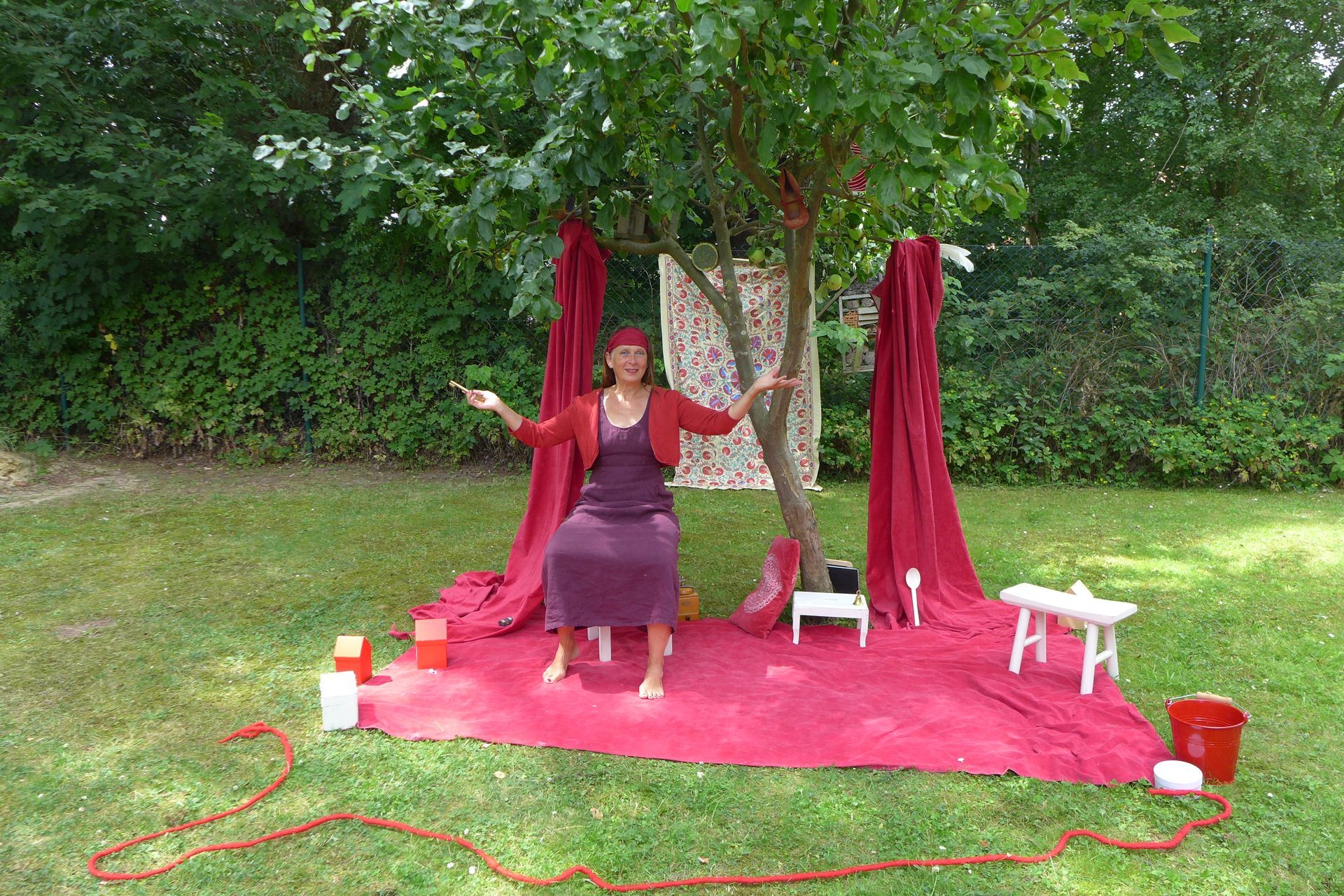 Eine Frau in einem lila Kleid sitzt mit ausgestreckten Armen unter einem Baum