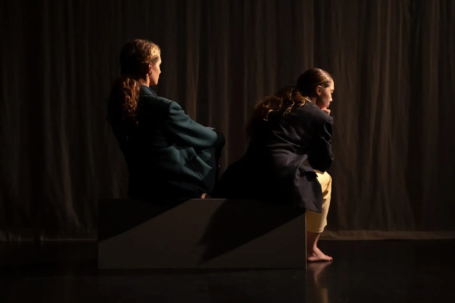 Zwei Frauen sitzen Rücken an Rücken in einem dunklen Raum