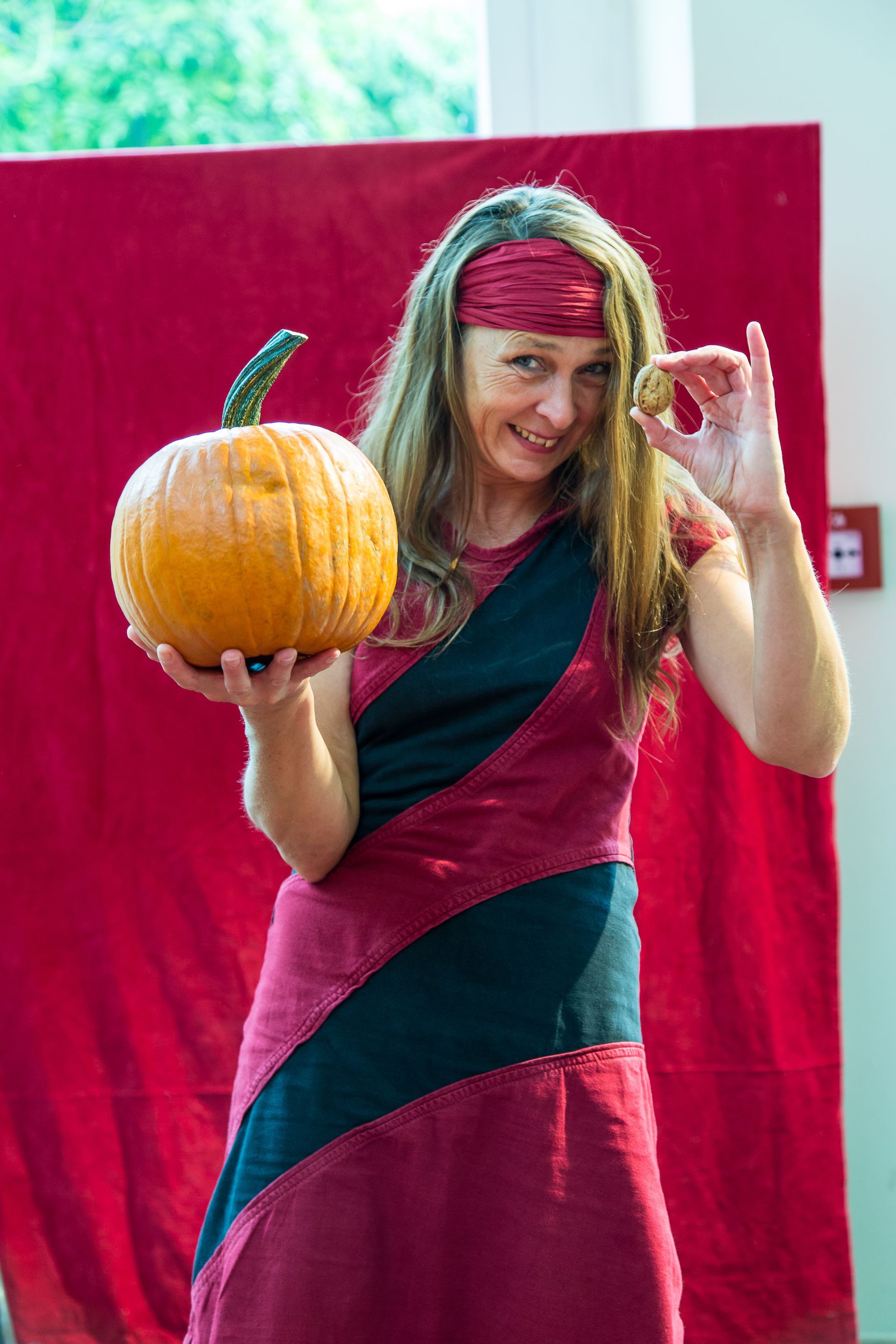 Eine Frau in einem rot-schwarzen Kleid hält einen Kürbis