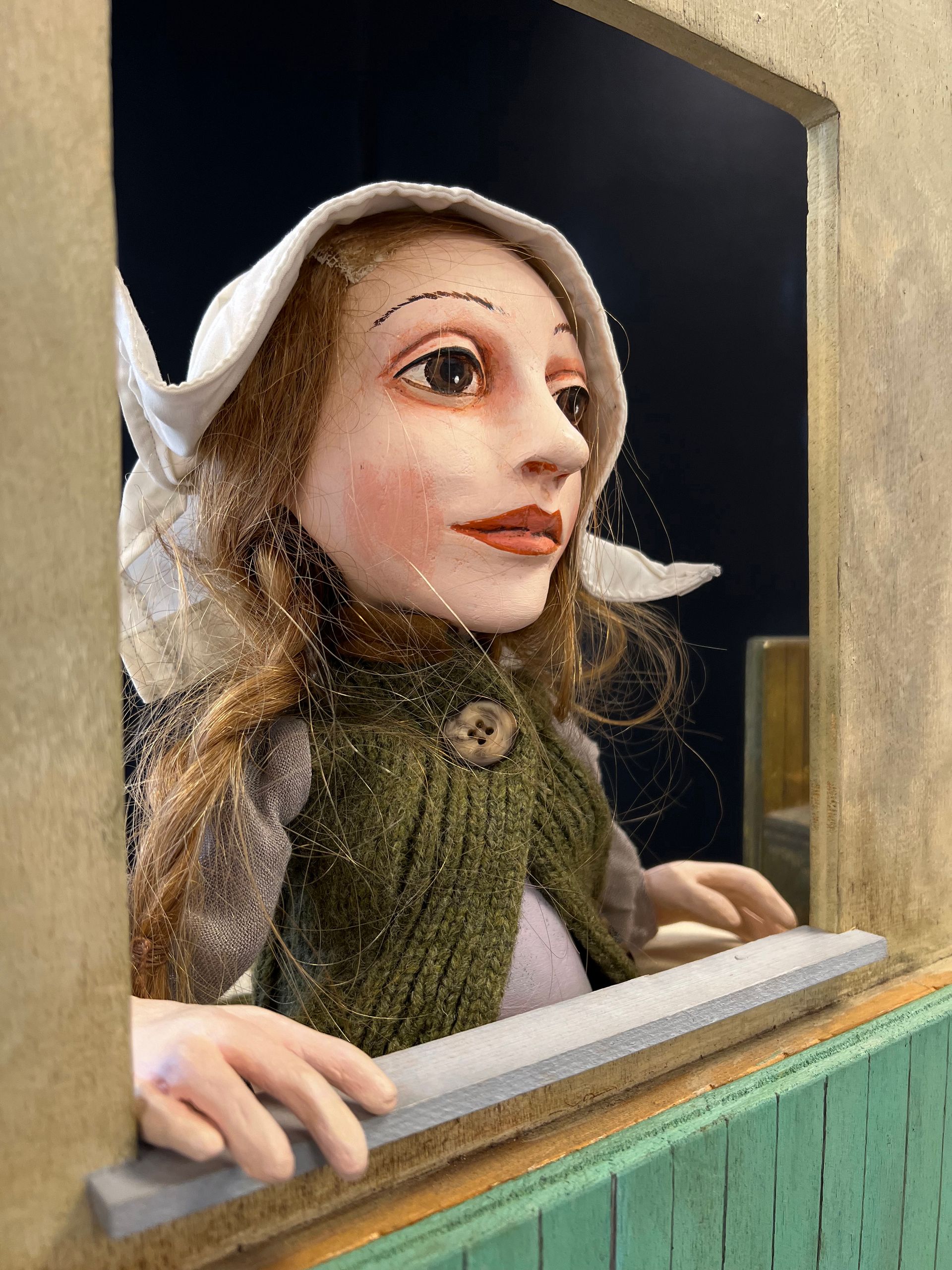 Eine Puppe mit einem weißen Hut schaut aus einem Fenster