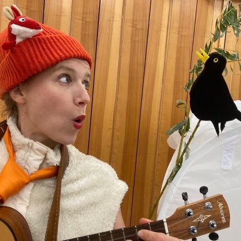 Eine Frau mit orangefarbenem Hut spielt Gitarre