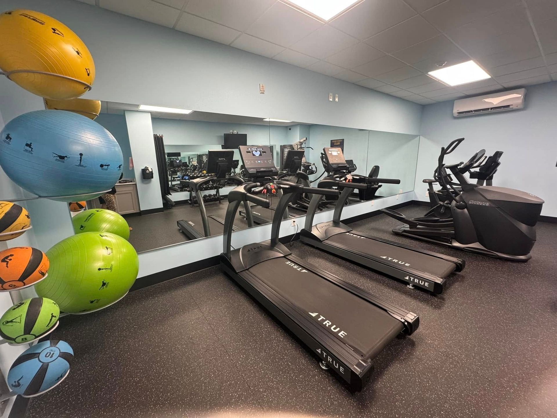 Gym interior with treadmills, elliptical, exercise balls, and mirrored wall.