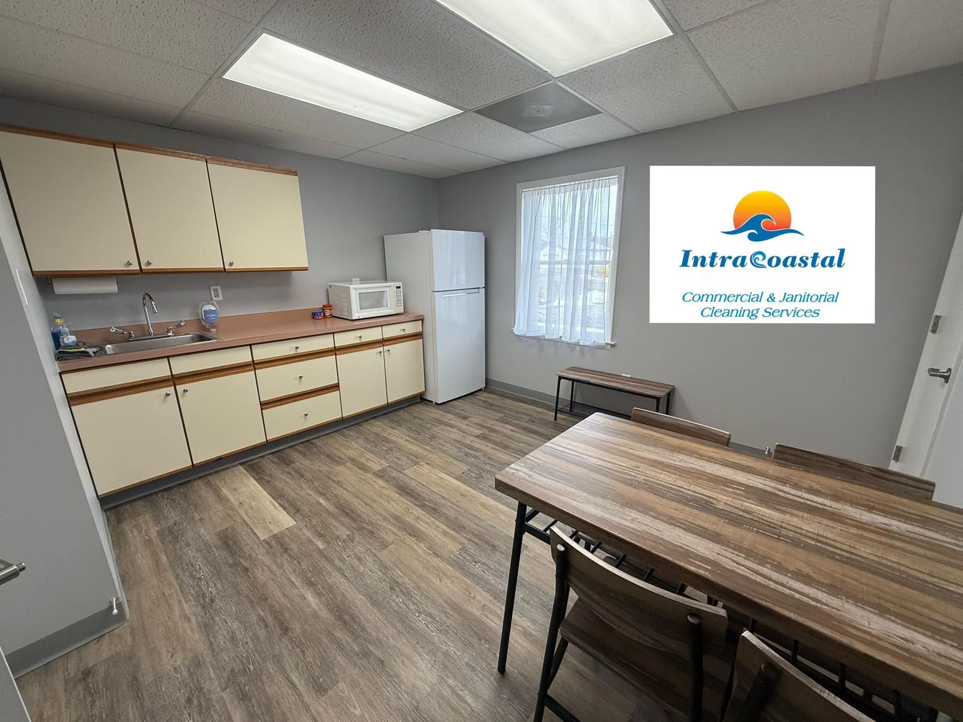 Kitchen with cabinets, fridge, microwave, and a table; IntraCoastal Construction & Janitorial Services logo on the wall.