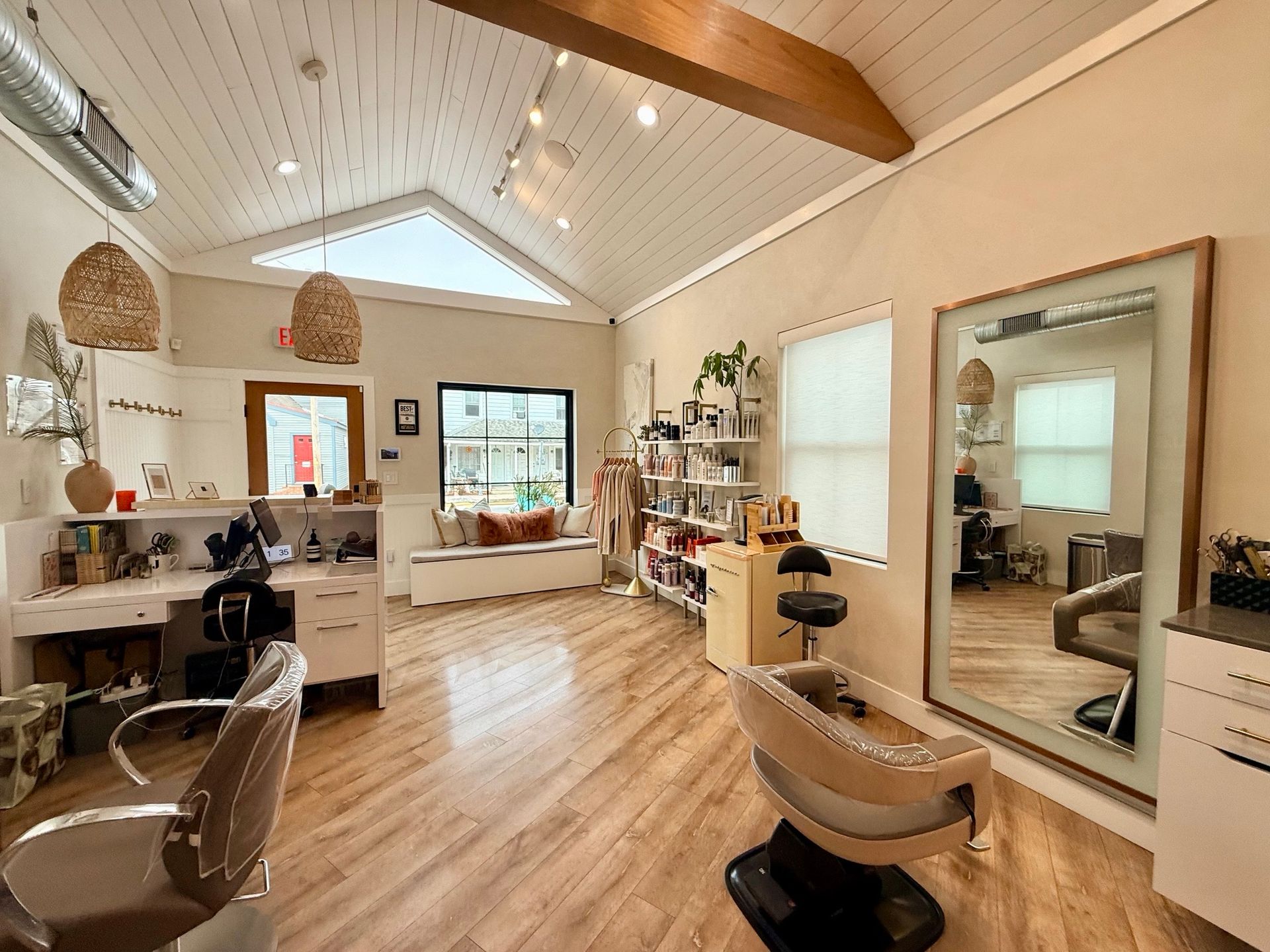 Hair salon interior with wood floors, neutral walls, vaulted ceiling, styling stations, and large mirrors.