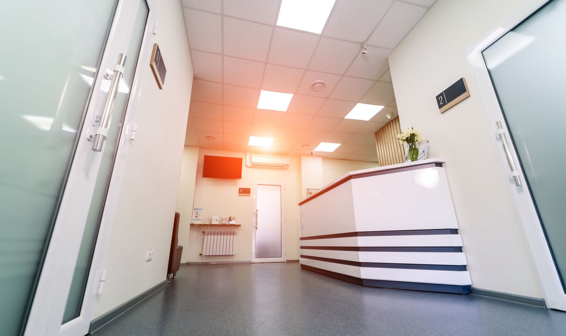 Brightly lit medical office reception area with white desk, doors, and walls.