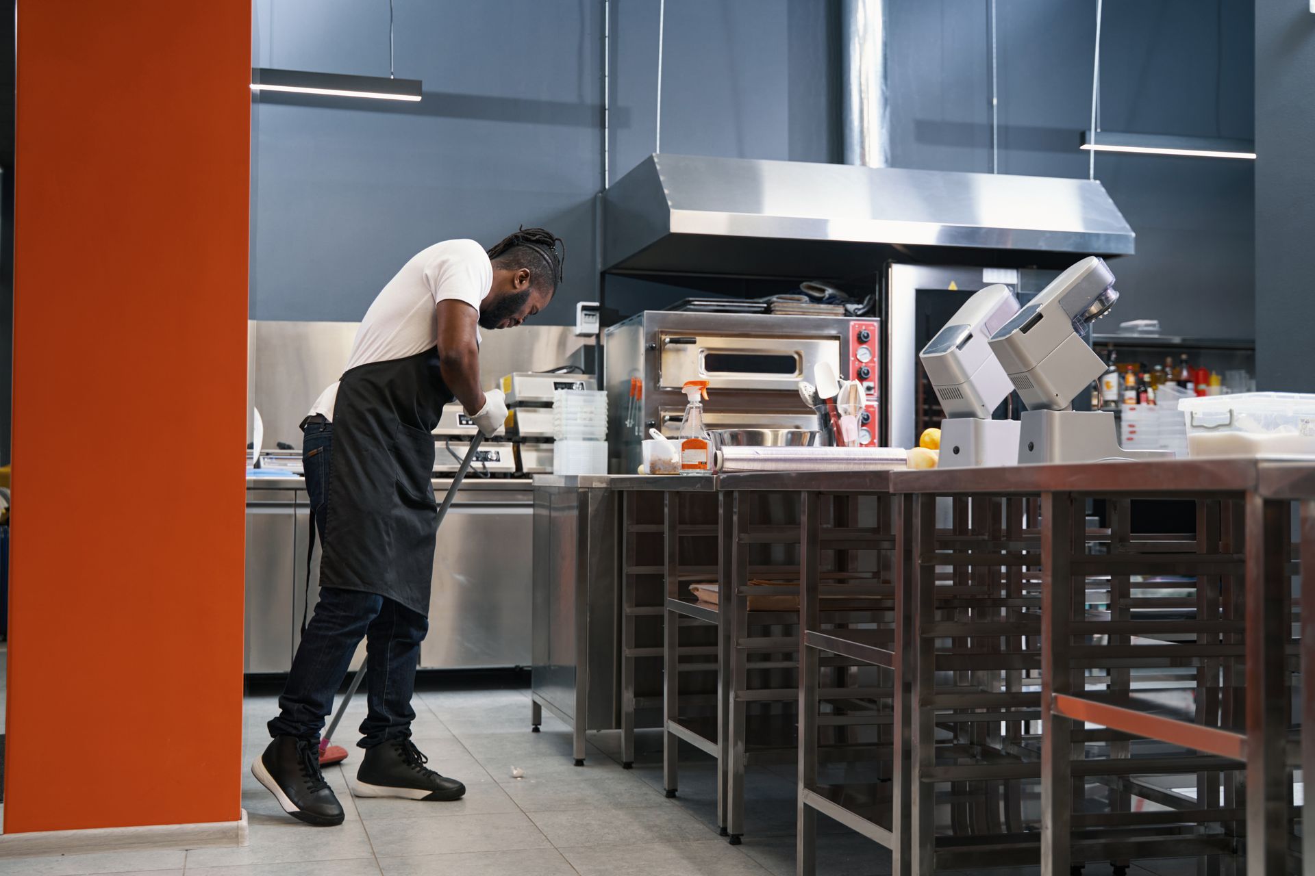 A person wearing an apron cleans a commercial kitchen. A person wearing an apron cleans a commercial kitchen.