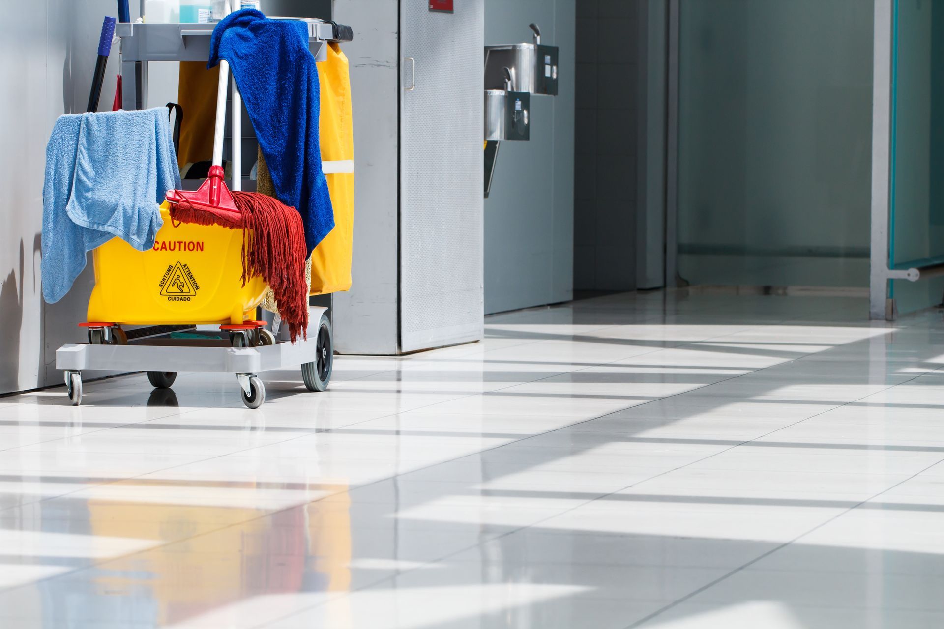 Cleaning cart with mop, rags, and bucket on a shiny floor in a hallway.