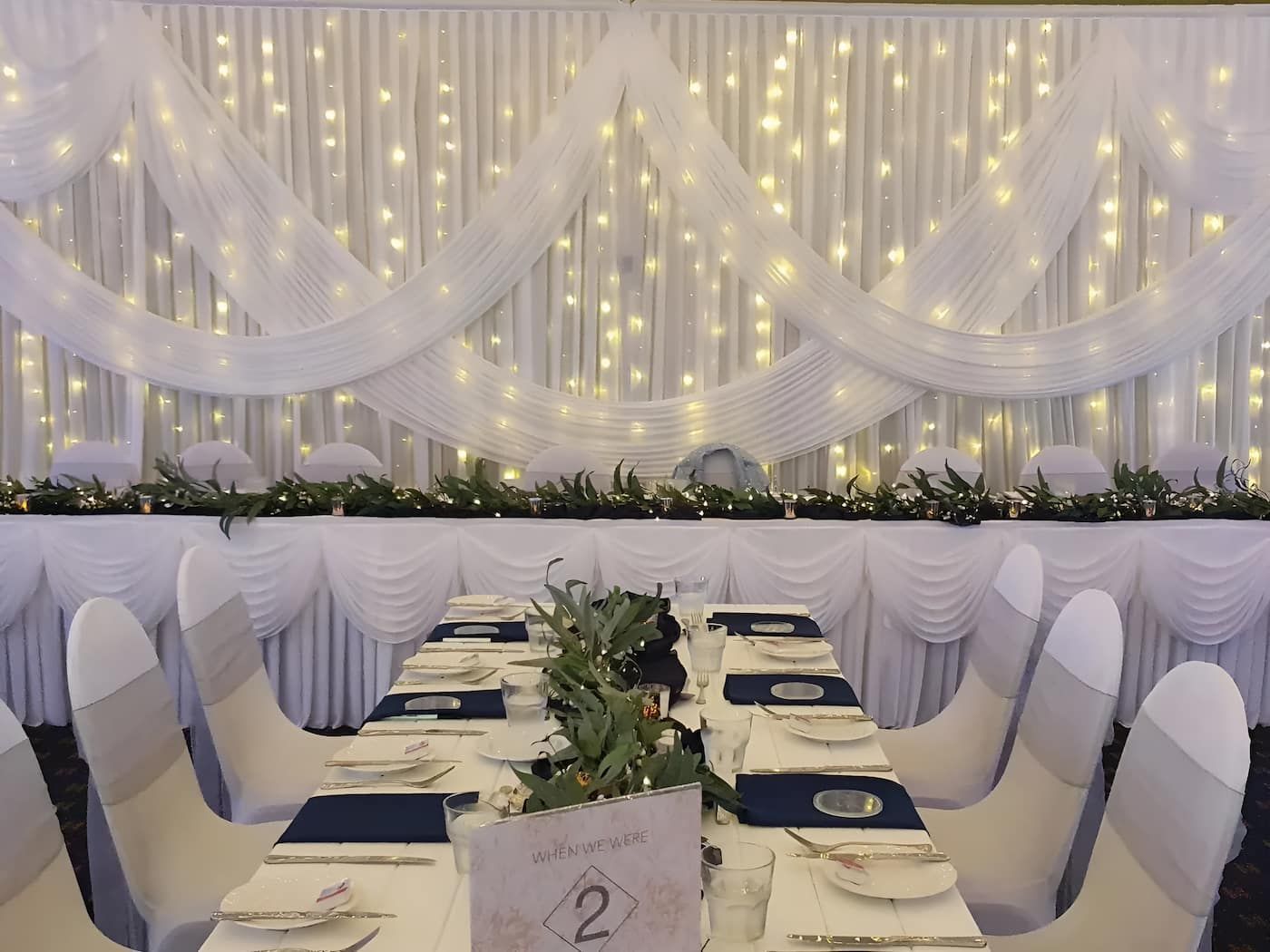 A Long Table Is Set For A Wedding Reception With A White Curtain Behind It — Lynda Ross Marriage Celebrant In Black River, QLD