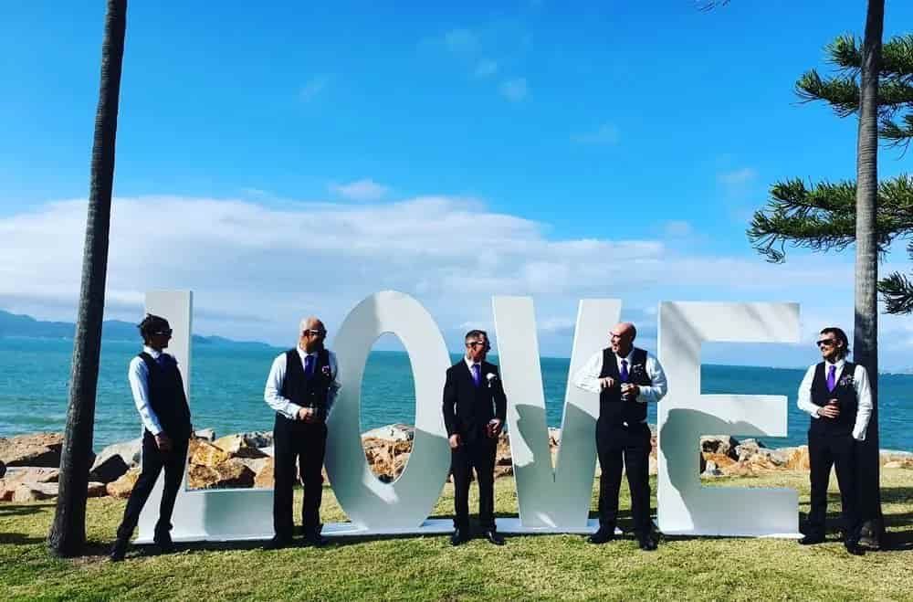 A Group Of Men Standing In Front Of A Large Love Sign — Lynda Ross Marriage Celebrant In Alice River, QLD