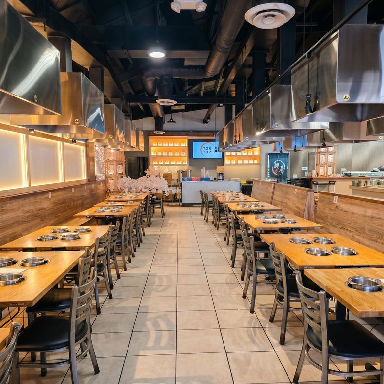 Empty modern restaurant interior with long wooden tables, metal stools, and warm wall lighting