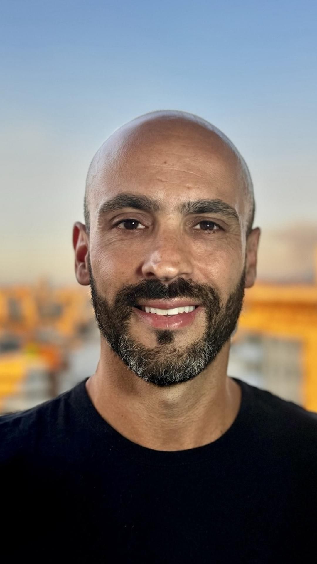Um homem careca com barba está sorrindo para a câmera.