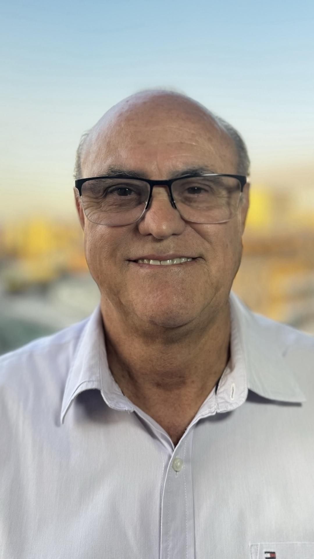 Um homem usando óculos e uma camisa branca está sorrindo para a câmera.