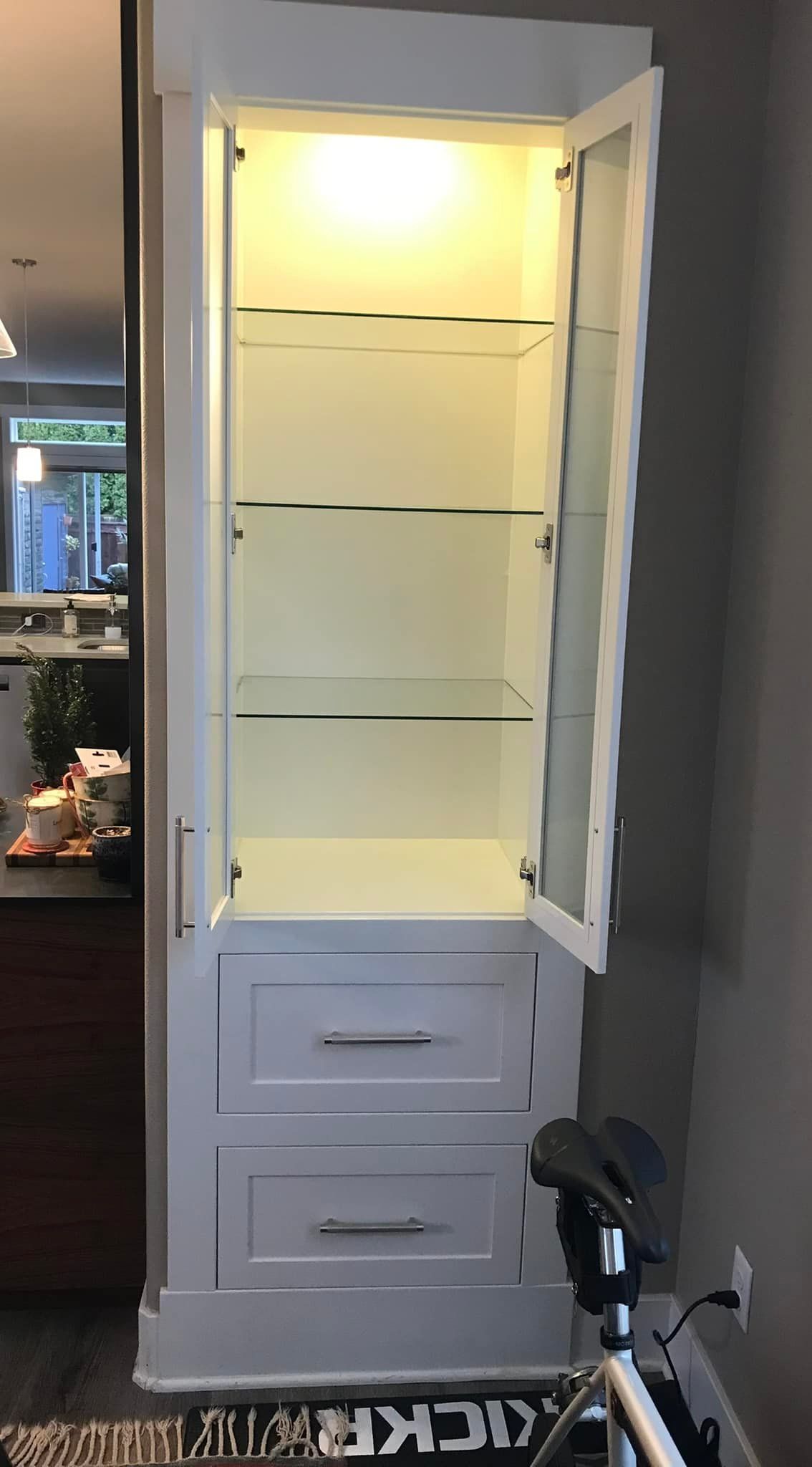 A white cabinet with a glass door and a bicycle in front of it.
