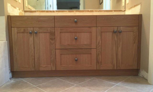 A bathroom vanity with wooden cabinets and drawers and a mirror.